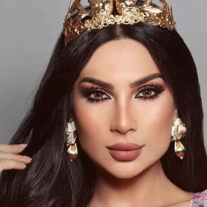 Woman wearing a gold crown and earrings against a gray background. Bella Glow Glow Radiant Hazelnut.