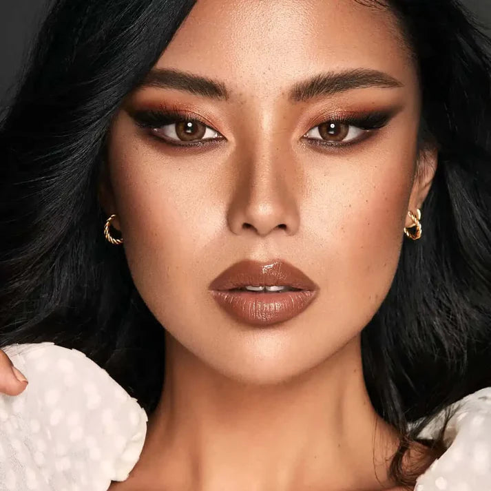 Close-up of a person with dark hair and makeup, wearing gold earrings. Bella_One_Day_Almond_Brown.
