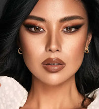 Close-up of a person with dark hair and makeup, wearing gold earrings. Bella_One_Day_Almond_Brown.