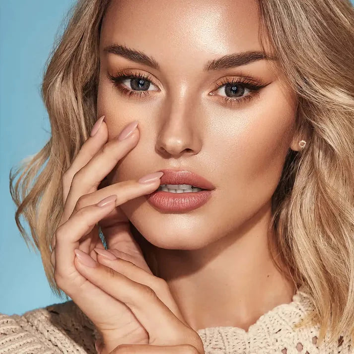Close-up of a woman with blonde hair and beige sweater against a blue. Bella One Day Ash Brown.